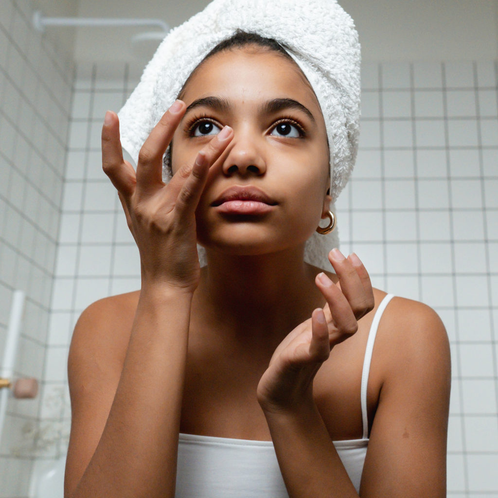 Woman applying skincare serums in white bathroom.